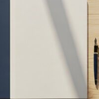 机の上に2冊の無地のフォルダとペン、観葉植物を並べた俯瞰イメージ。特定技能1号と2号という2つの段階を象徴。