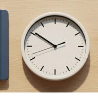 机の上にノートとペン、文字盤が無地の時計、観葉植物を並べた俯瞰イメージ。資格外活動許可の週28時間の管理を象徴。
