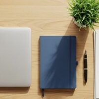机の上に閉じたノートパソコンとノート、ペン、観葉植物を並べた俯瞰イメージ。オンラインで在留申請の準備をする様子を象徴。