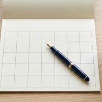 在留期間の更新をいつ申請するか計画することを象徴する、白紙のカレンダーとペンが机に置かれた俯瞰イメージ