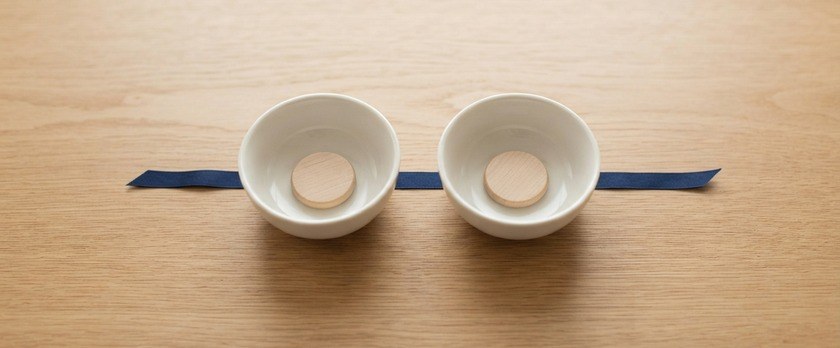 白い器を2つ並べ、それぞれに木の駒を1つずつ置いて紺色のリボンでつないだ俯瞰イメージ。減額には2つの要件の両方が必要であることを象徴。