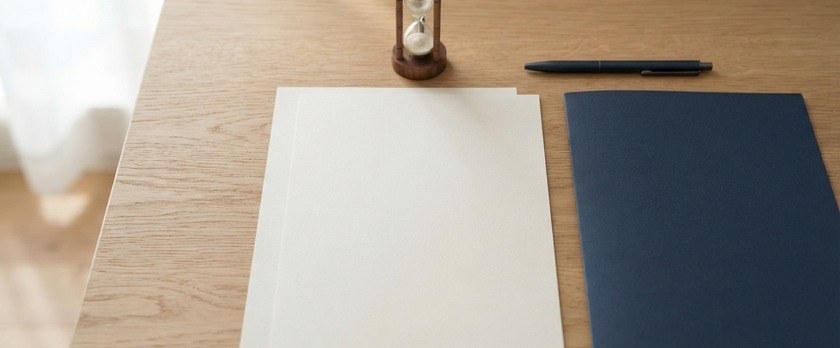 少しずらして重ねた無地の書類と紺色のフォルダ、砂時計の俯瞰イメージ。特別養子縁組の審判と確定後の届出を象徴。