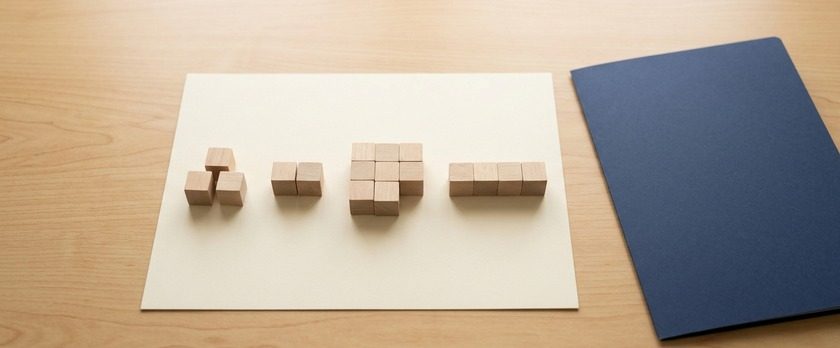 無地の木製ブロックを大きさの違う塊に分けて並べた俯瞰イメージ。分野ごとに必要な指導対象者数が異なることを象徴。
