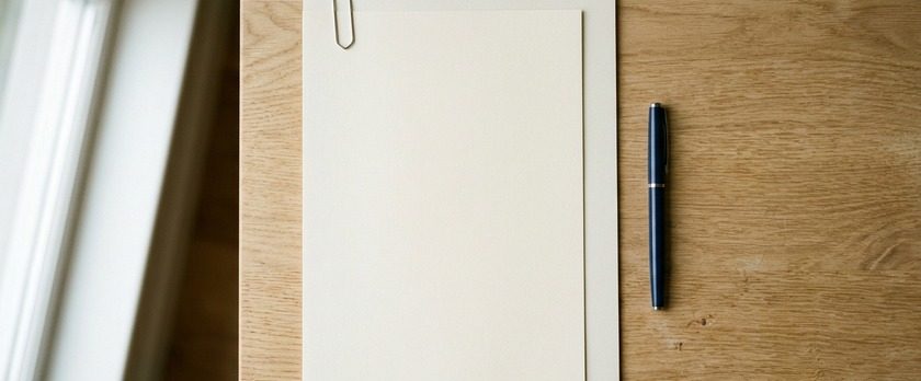 無地の書類の後ろに少し小さな無地の紙を重ねてクリップで留めた俯瞰イメージ。外国語の証明書に日本語訳を添えて提出することを象徴。