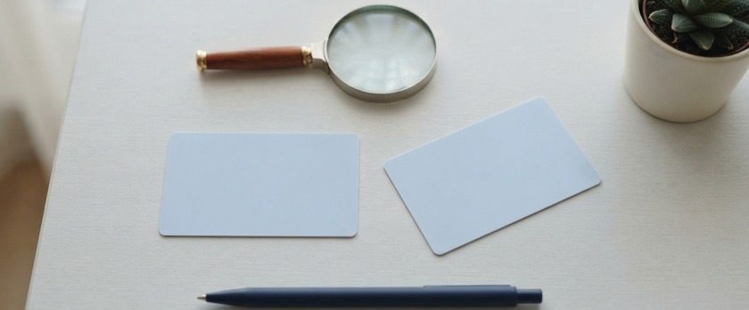 無地のカード2枚と虫めがねを並べた俯瞰イメージ。在留カードの表面と裏面の両方を確認することを象徴。