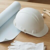 木の机に白いヘルメット、無地の図面用紙、白い作業手袋を並べた俯瞰イメージ。宮崎の特定技能・建設分野を象徴。