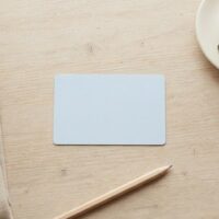 カフェのカウンターに無地のカードとエプロン、コーヒーカップを並べた俯瞰イメージ。家族滞在の方がパートで働けるかという問いを象徴。