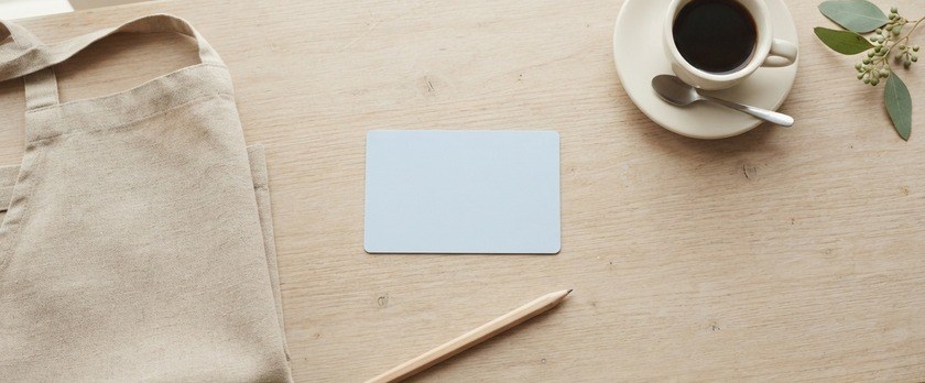 カフェのカウンターに無地のカードとエプロン、コーヒーカップを並べた俯瞰イメージ。家族滞在の方がパートで働けるかという問いを象徴。