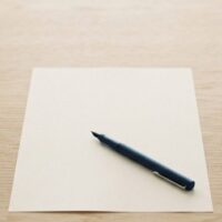 離して置いた2つの無地のカップと、その間の無地の書類とペンの俯瞰イメージ。国際離婚の届出手続を象徴。