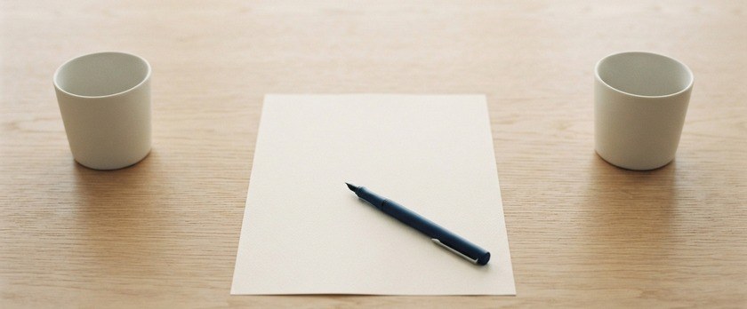 離して置いた2つの無地のカップと、その間の無地の書類とペンの俯瞰イメージ。国際離婚の届出手続を象徴。