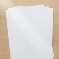 木の机に白紙の用紙と鉛筆、木の駒を入れた白い器を並べた俯瞰イメージ。日本語能力の証明に向けた試験の準備を象徴。