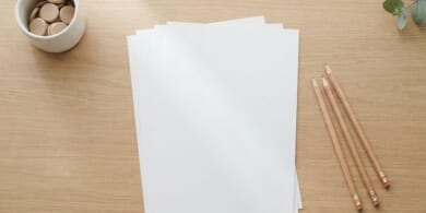 木の机に白紙の用紙と鉛筆、木の駒を入れた白い器を並べた俯瞰イメージ。日本語能力の証明に向けた試験の準備を象徴。