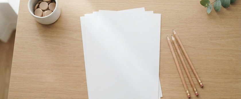 木の机に白紙の用紙と鉛筆、木の駒を入れた白い器を並べた俯瞰イメージ。日本語能力の証明に向けた試験の準備を象徴。