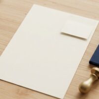 白紙の書類に小さな付箋状の紙を重ねた俯瞰イメージ。アポスティーユが公文書に付箋で付与されることを象徴。