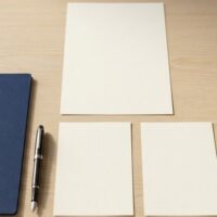 白紙の書類1枚の下に2枚を並べた俯瞰イメージ。特定技能2号が複数の作業員を指導する立場であることを象徴。