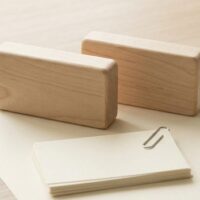 無地の木のプレート2つを前後に並べ、その下に留め具でまとめた無地の紙束を置いた俯瞰イメージ。看板が変わっても足元の書類はそのままであることを象徴。