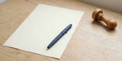 白紙の書類の上にペンが置かれ、少し離れたところに無地の木製印鑑が横向きに置かれた俯瞰イメージ。海外在住者は印鑑証明に代えて署名証明を使うことを象徴。