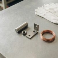 作業台の上に無地の金属部品と銅線、白い作業手袋を並べた俯瞰イメージ。宮崎の特定技能・工業製品製造業分野を象徴。