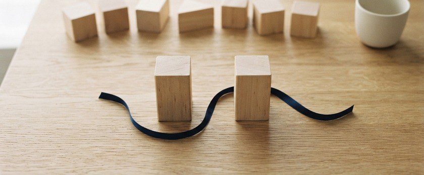 ほぼ同じ高さの木のブロック2個の間に紺色のリボンを添えたイメージ。建設と外食業など、分野別の順位が入れ替わったことを象徴。