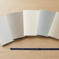 無地のフォルダを6つ並べ、紺色のリボンとペンを添えた机のイメージ。育成就労の協力覚書が6か国になったことを象徴。