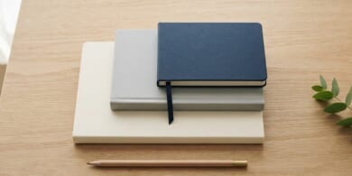 表紙が無地のノート3冊を階段のように少しずつずらして重ね、紺色のしおりひもを垂らした俯瞰イメージ。日本語能力の水準が一段上がることを象徴。