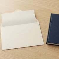 開いた無地の封筒と折りたたんだ書類、紺色のノートとペンの俯瞰イメージ。通知を落ち着いて読み、説明を受ける前に質問を準備することを象徴。