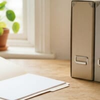 無地の保存箱と開いたファイルを置いた机のイメージ。保管されている過去の記録の取り寄せを象徴。
