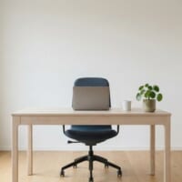 窓から光が入る小さな事務所に、木の机と椅子、観葉植物を置いたイメージ。事業所の確保を象徴。