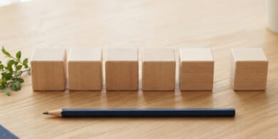 無地の木のキューブ5個を一列に並べ、少し離して6個目を置いた俯瞰イメージ。特定技能1号の通算5年と、6年まで延びる取扱いを象徴。