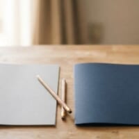 灰色と紺色の無地のフォルダーを並べた机のイメージ。今の在留資格から別の在留資格へ変更する手続を象徴。