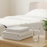 明るい介護施設の居室に、たたんだタオルと水のグラス、観葉植物を置いたイメージ。介護の現場を象徴。