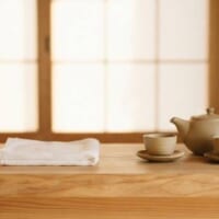 木のカウンターに呼び鈴と白いタオル、急須を置いた旅館の受付のイメージ。育成就労の宿泊分野を象徴。