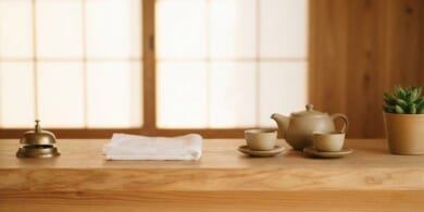 木のカウンターに呼び鈴と白いタオル、急須を置いた旅館の受付のイメージ。育成就労の宿泊分野を象徴。