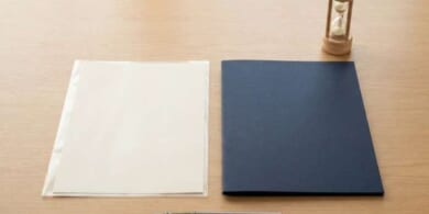 透明ファイルに入れた無地の書類と紺色のフォルダ、木の砂時計の俯瞰イメージ。入国前に期限内で準備する結核非発病証明書を象徴。